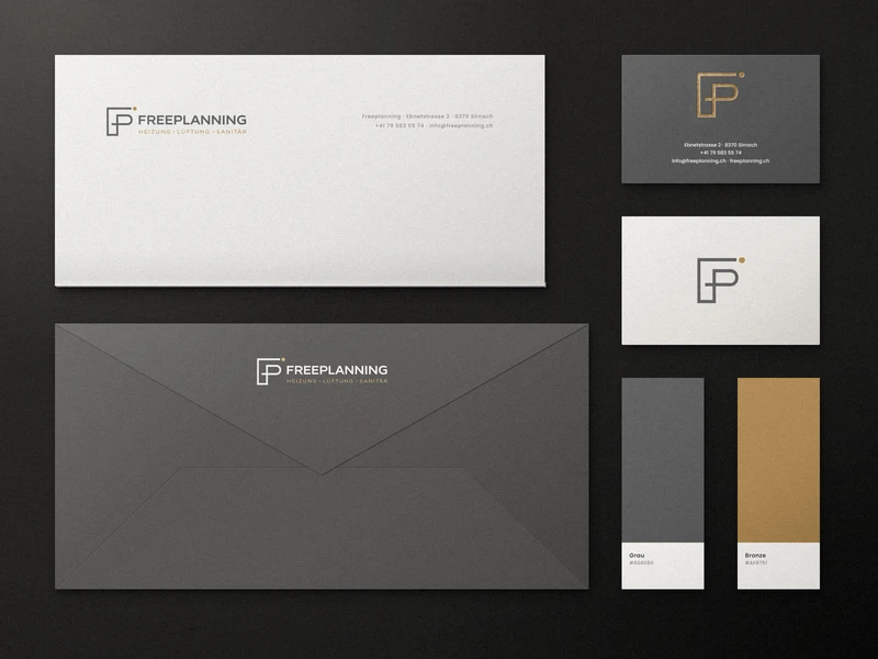 Freeplanning stationery on a dark surface: folded letterhead with logo, grey envelope with logo on the flap, dark business card with gold-foil mark and contact details, light business card with the mark, and two colour swatches in grey and bronze.
